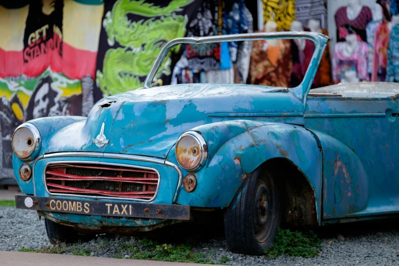 an old blue car is in front of a mural