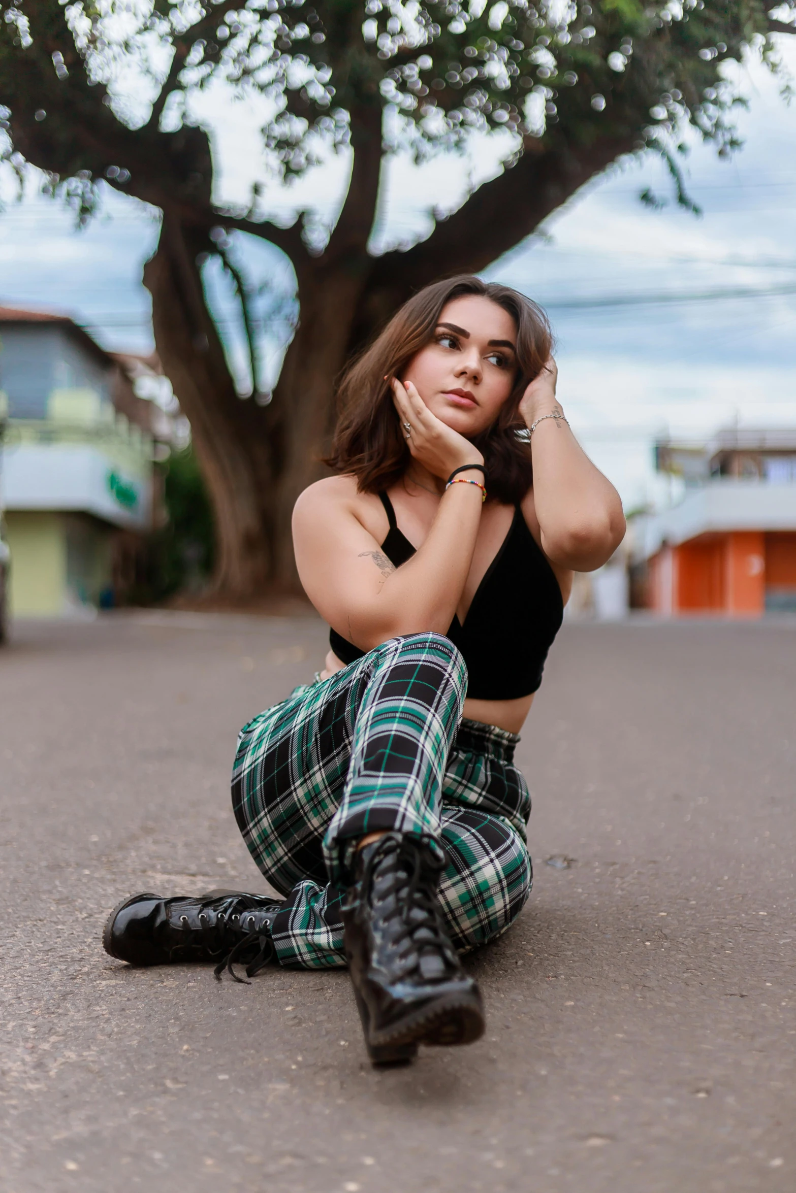 woman sitting on a street corner in black top with plaid pants and high boots