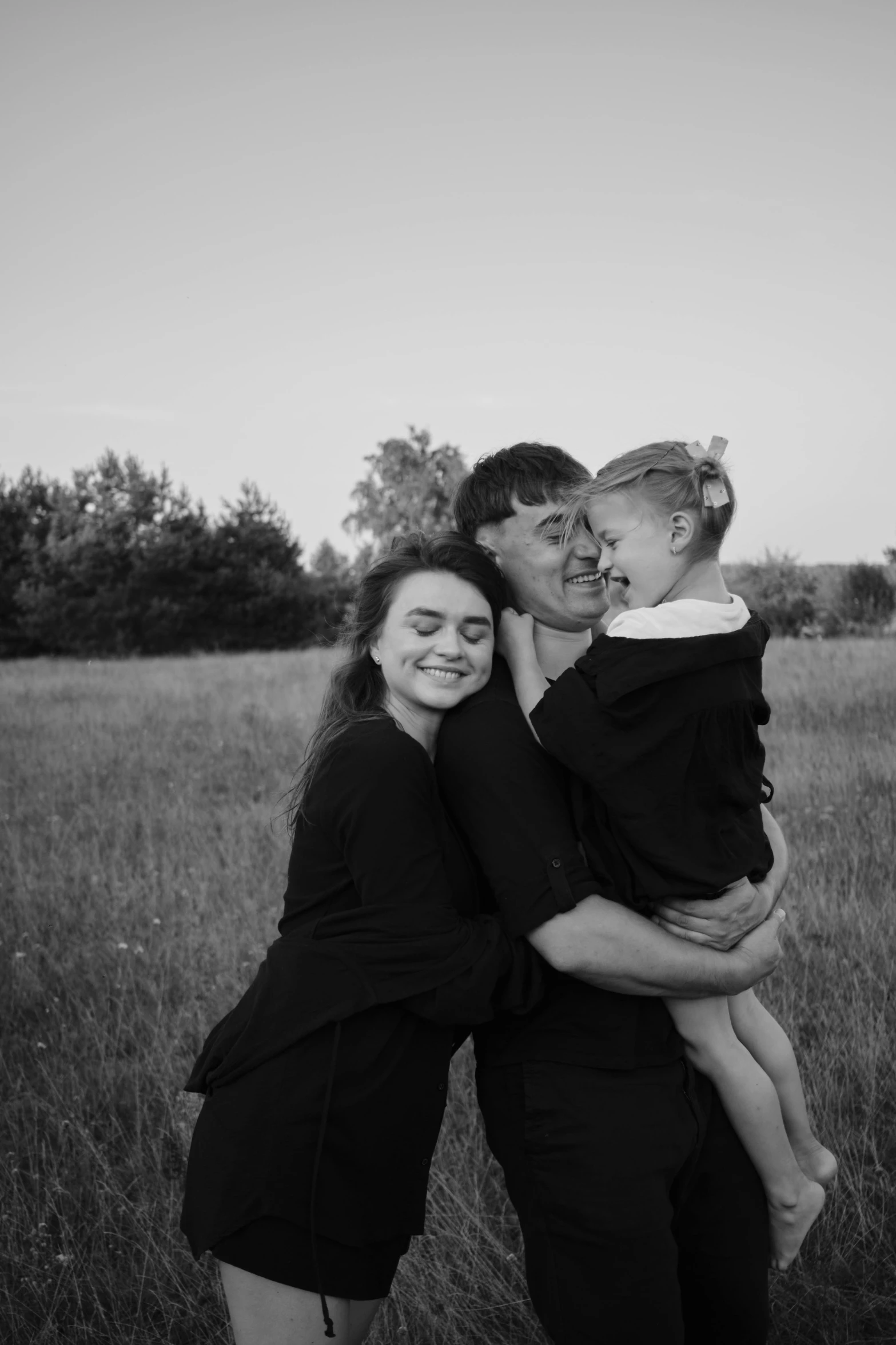 three adults and two children hug in a field