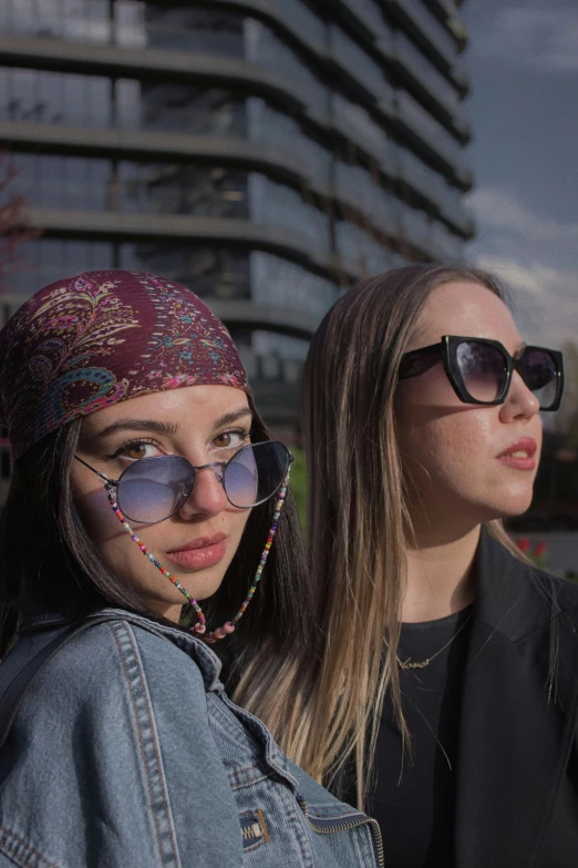 two girls pose for the camera, in front of some very tall buildings