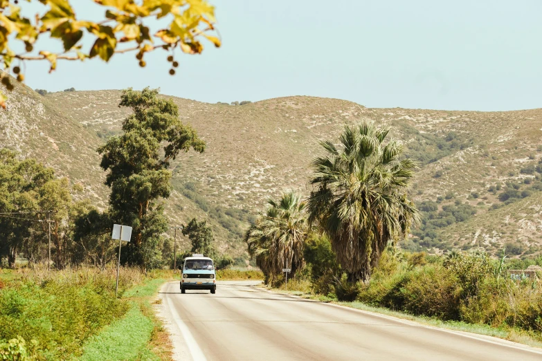 a car traveling down the road with hills behind