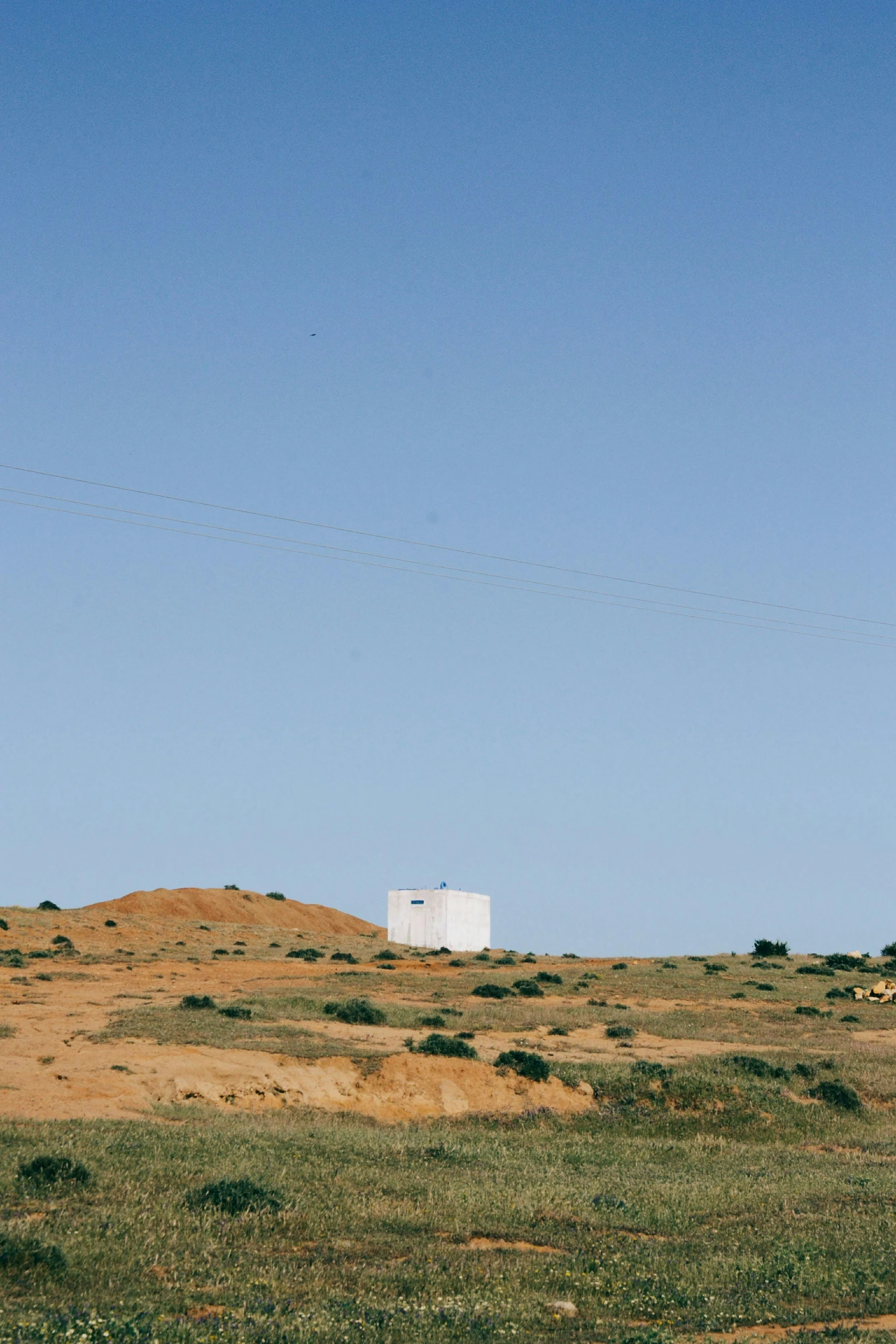 a small white structure sitting on a hill surrounded by grass