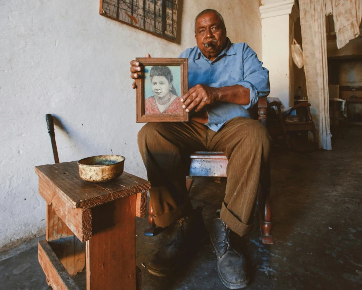 a man holding up an old picture frame with a portrait of a woman