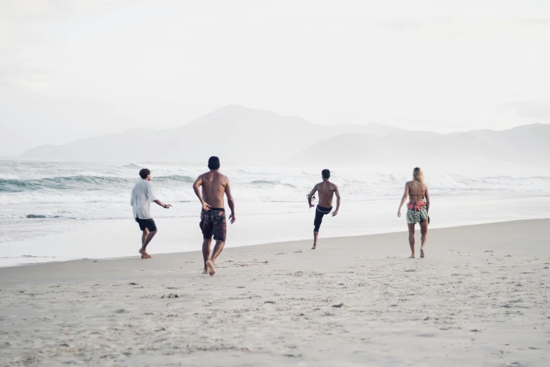 four men are walking along the beach in their bathing suits