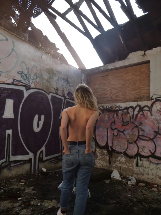 a girl stands against the side of a graffiti wall