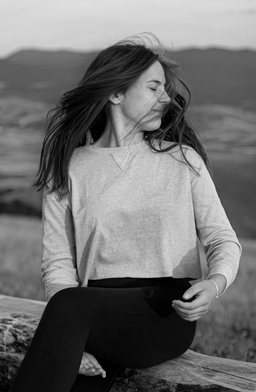 a woman sitting on a log outside looking off into the distance