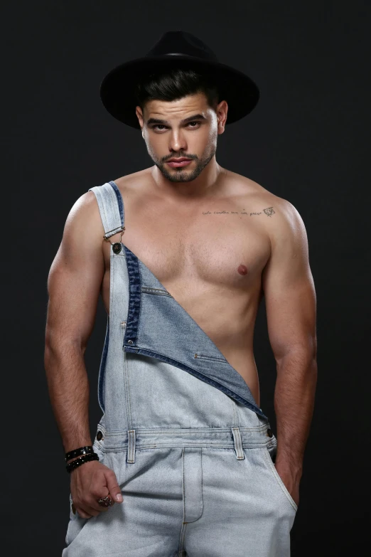 a shirtless young man posing in overalls and hat