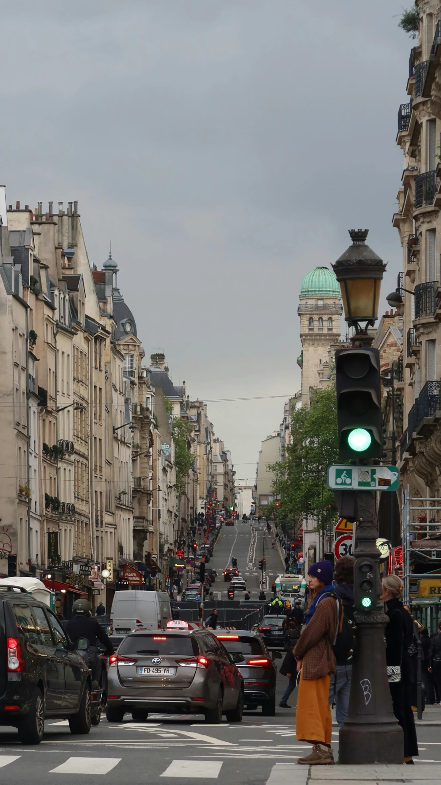 several people walking on a street near many parked cars