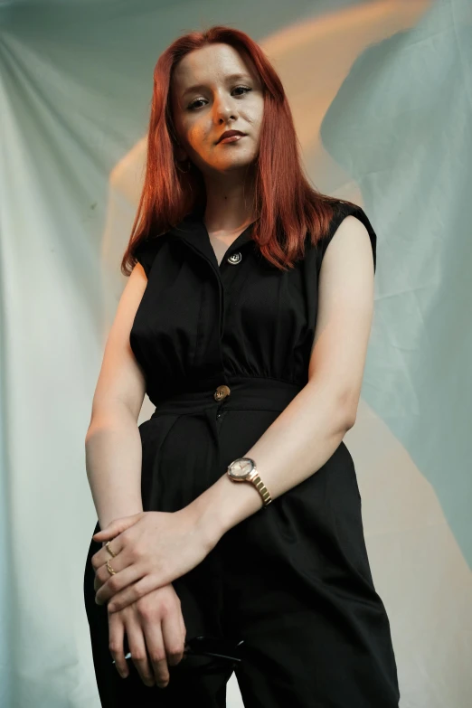 red headed woman posing against a white backdrop with her hand on her hips