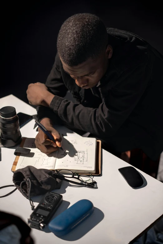 a man writing on paper next to camera equipment