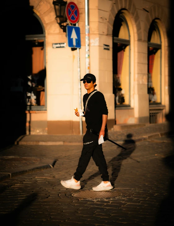 man in black walking on street holding a cigarette and wearing sunglasses