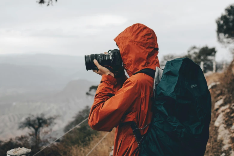 a man with an orange raincoat on and a camera taking a po