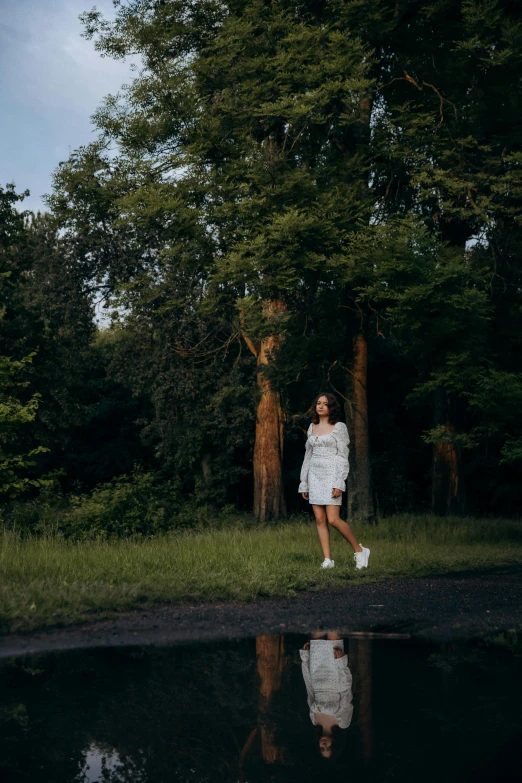 a woman in a white dress standing near trees and a body of water