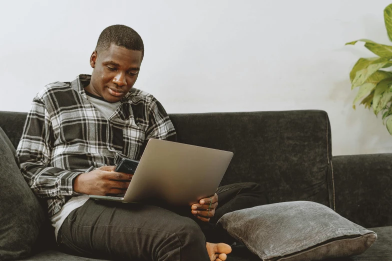 a man sitting on top of a couch looking at a laptop