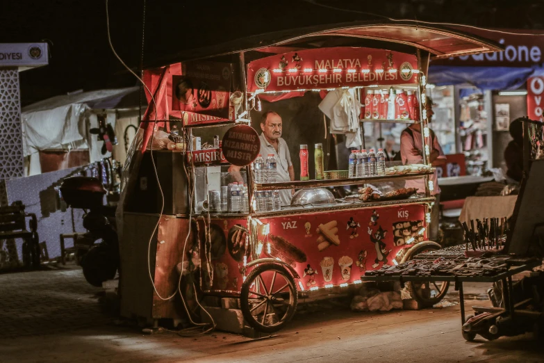 a food cart is lit up at night with people walking around