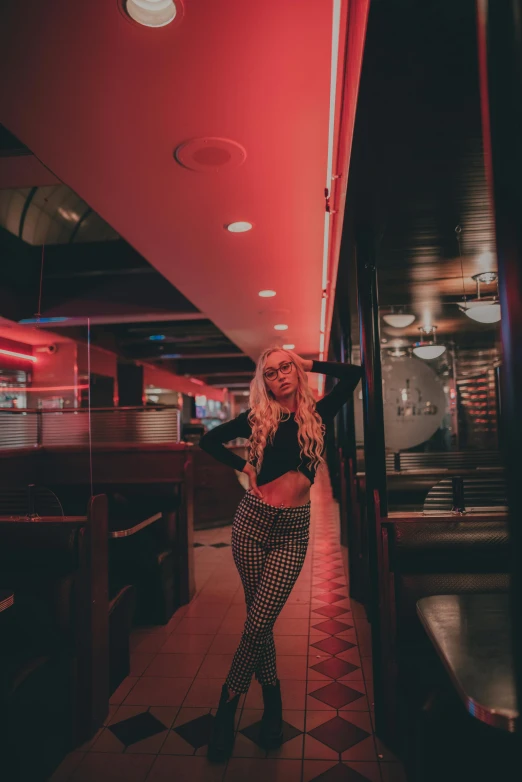 a beautiful blonde woman wearing plaid pants and black shirt standing in an empty restaurant