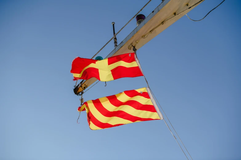 two red and yellow flag hanging from the top of a ship