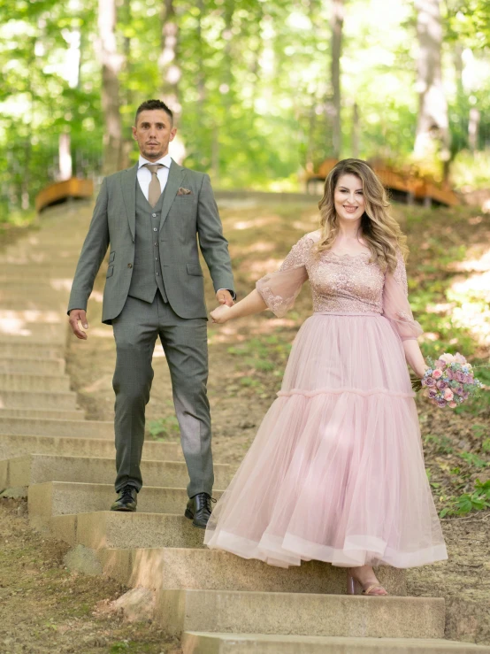 a woman in a pink dress walking down steps next to a man in grey suit