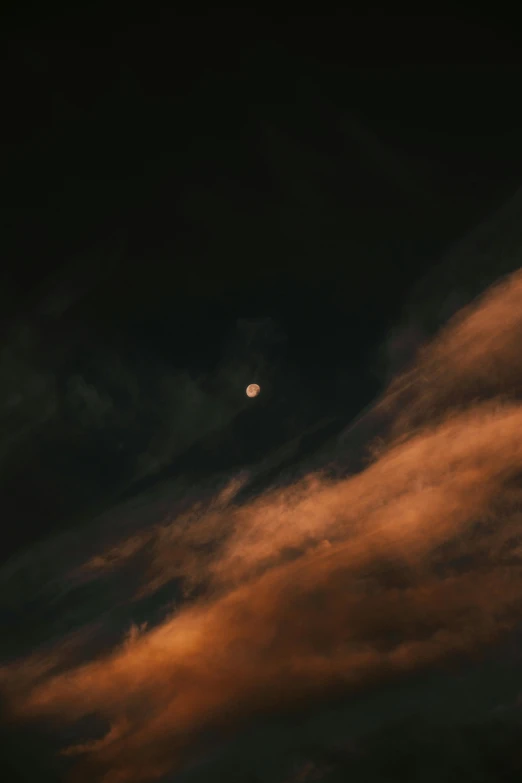 the moon is seen in the distance as dark clouds drift overhead