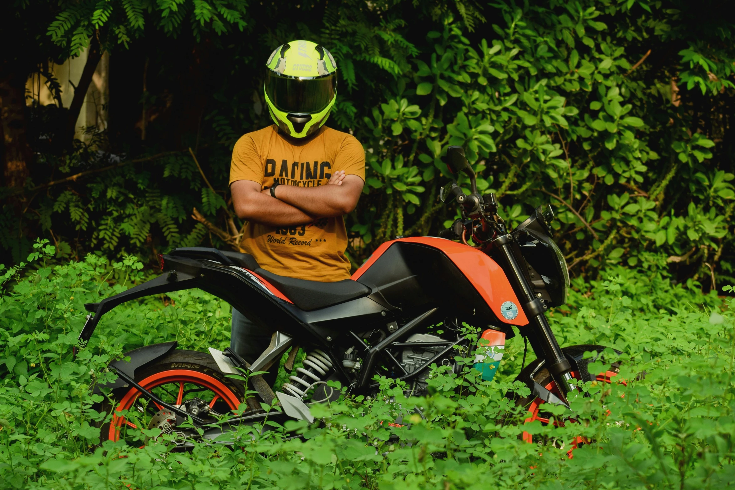 a man sitting on an orange motorcycle with his arms crossed in grass