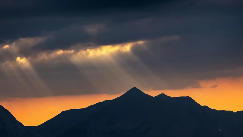 the sunbeames break behind the mountains in a hazy sky