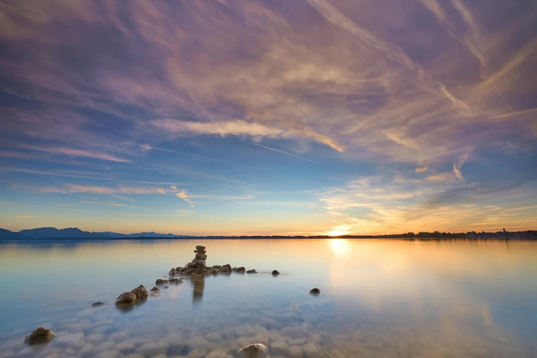 a body of water with rocks in the middle and a setting sun above