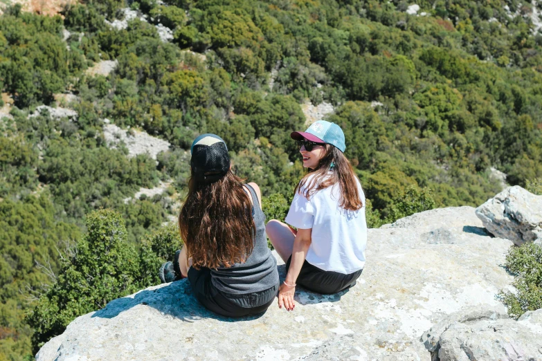 two women sitting on a rock at the top of a mountain