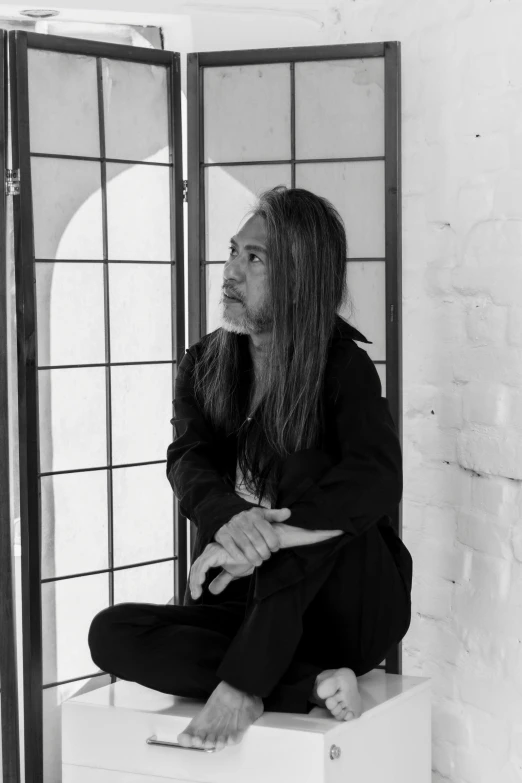 a man with long hair sitting down with his feet crossed