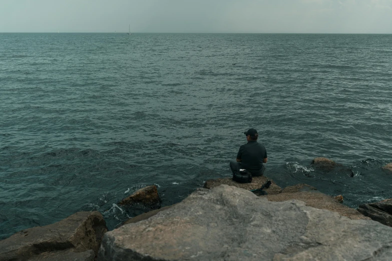 a person sitting on top of a rocky cliff next to the ocean