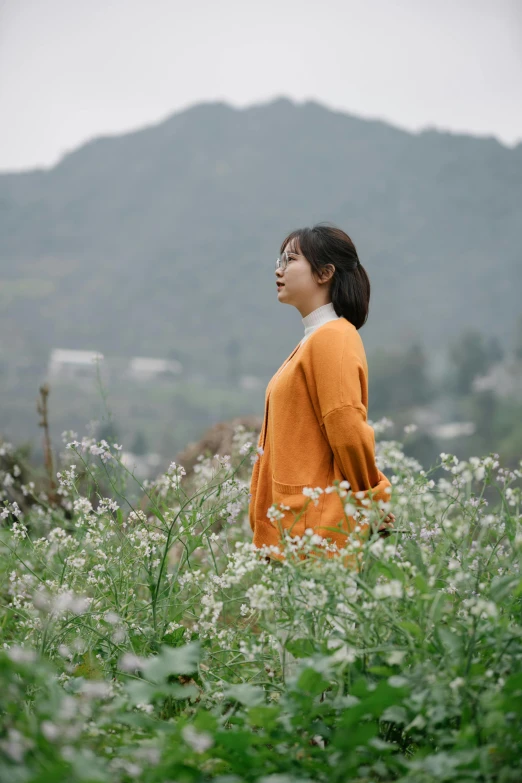 a woman standing in tall grass with hills in the background