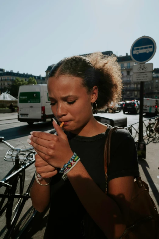 a woman is standing by a bicycle on the street smoking a cigarette