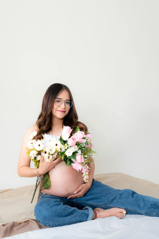 a pregnant woman with glasses holding flowers and posing for the camera