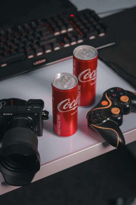 two can of soda, a camera, and a video game controller on a desk