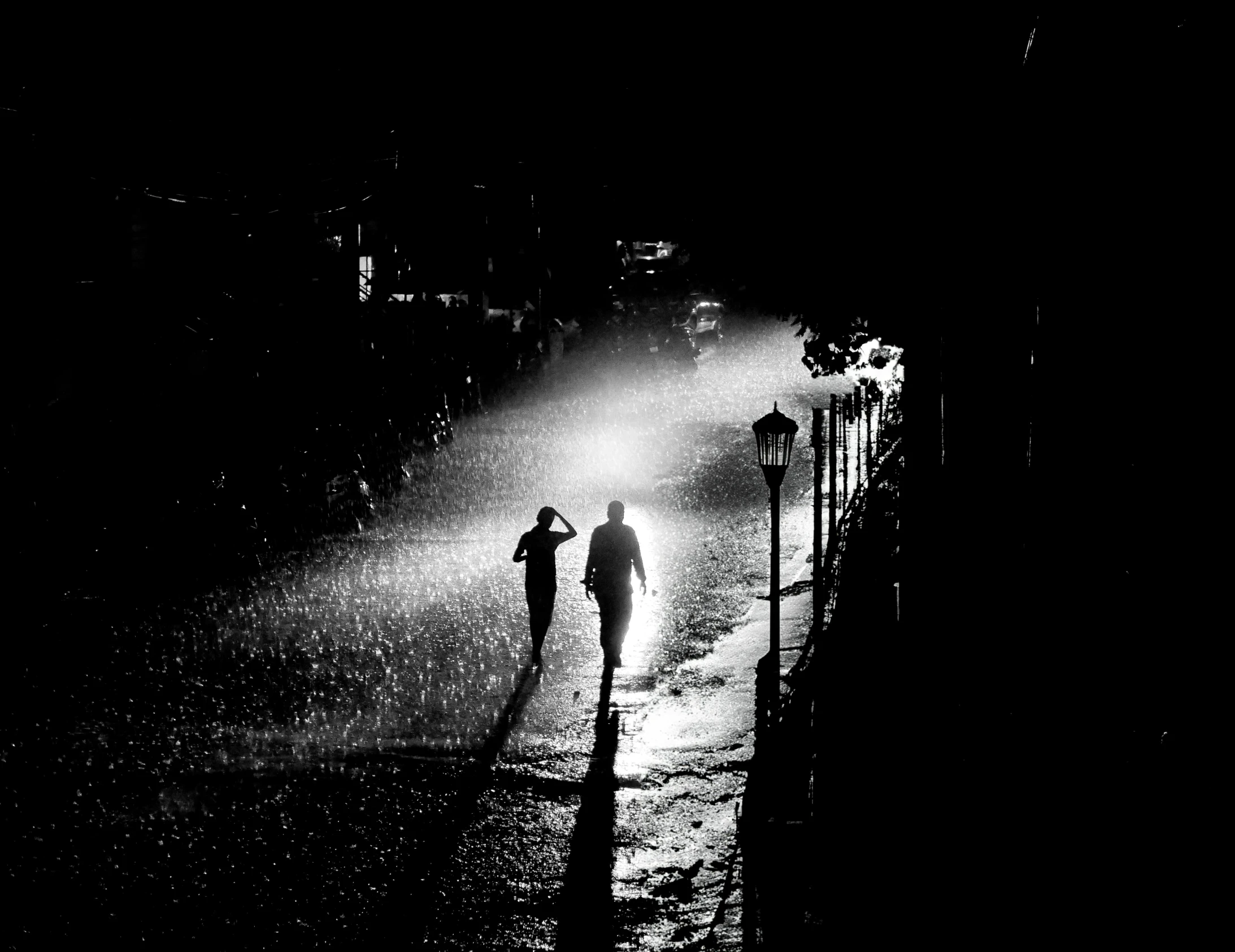 a couple of people walking up a street next to a fence