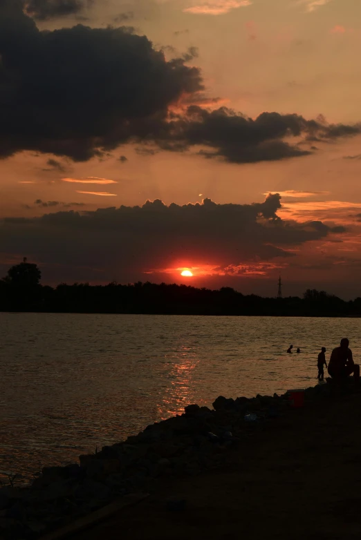 a couple of people sitting at the water watching the sun rise