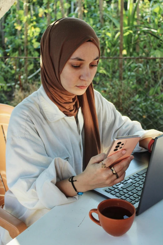 a girl sitting in front of her laptop looking at her cellphone