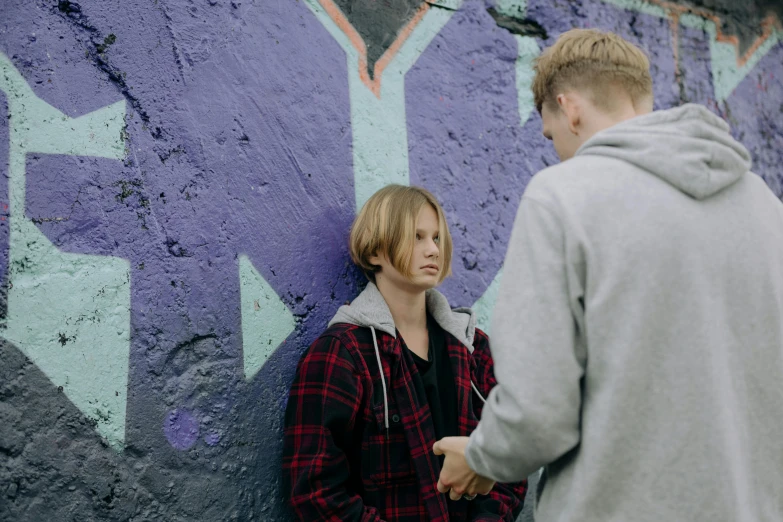 two people standing near a purple wall covered with graffiti