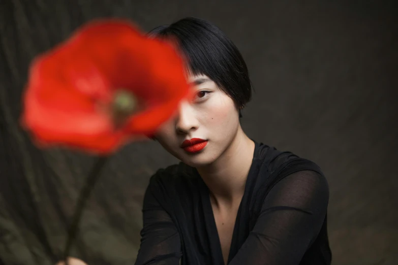 an oriental woman holding a red flower near her face