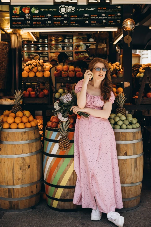 woman in sunglasses stands outside a market selling fresh fruit