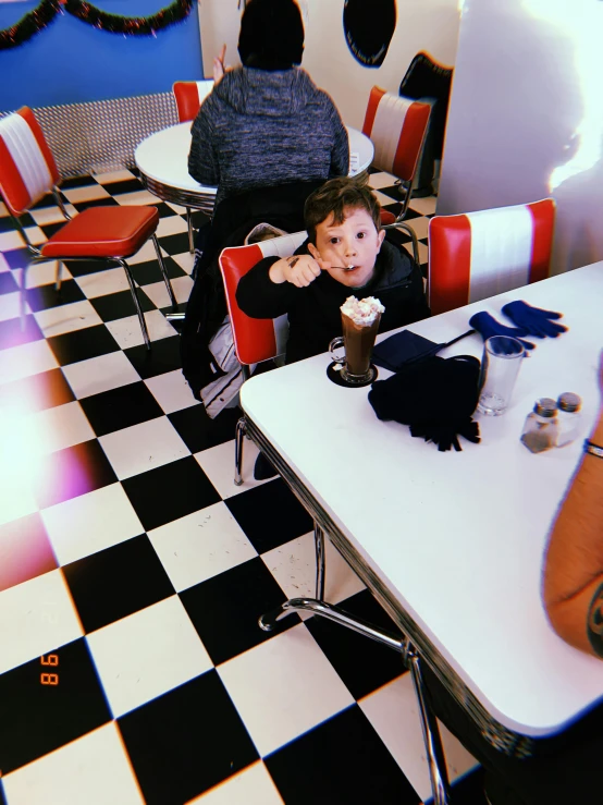 a little girl sitting at a table with a cup of ice cream