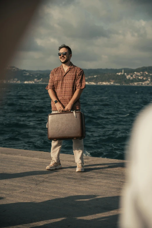 a man with shades holding a suitcase on a pier