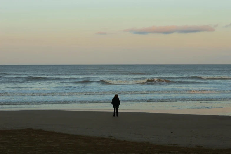 two people stand on the beach, facing the ocean