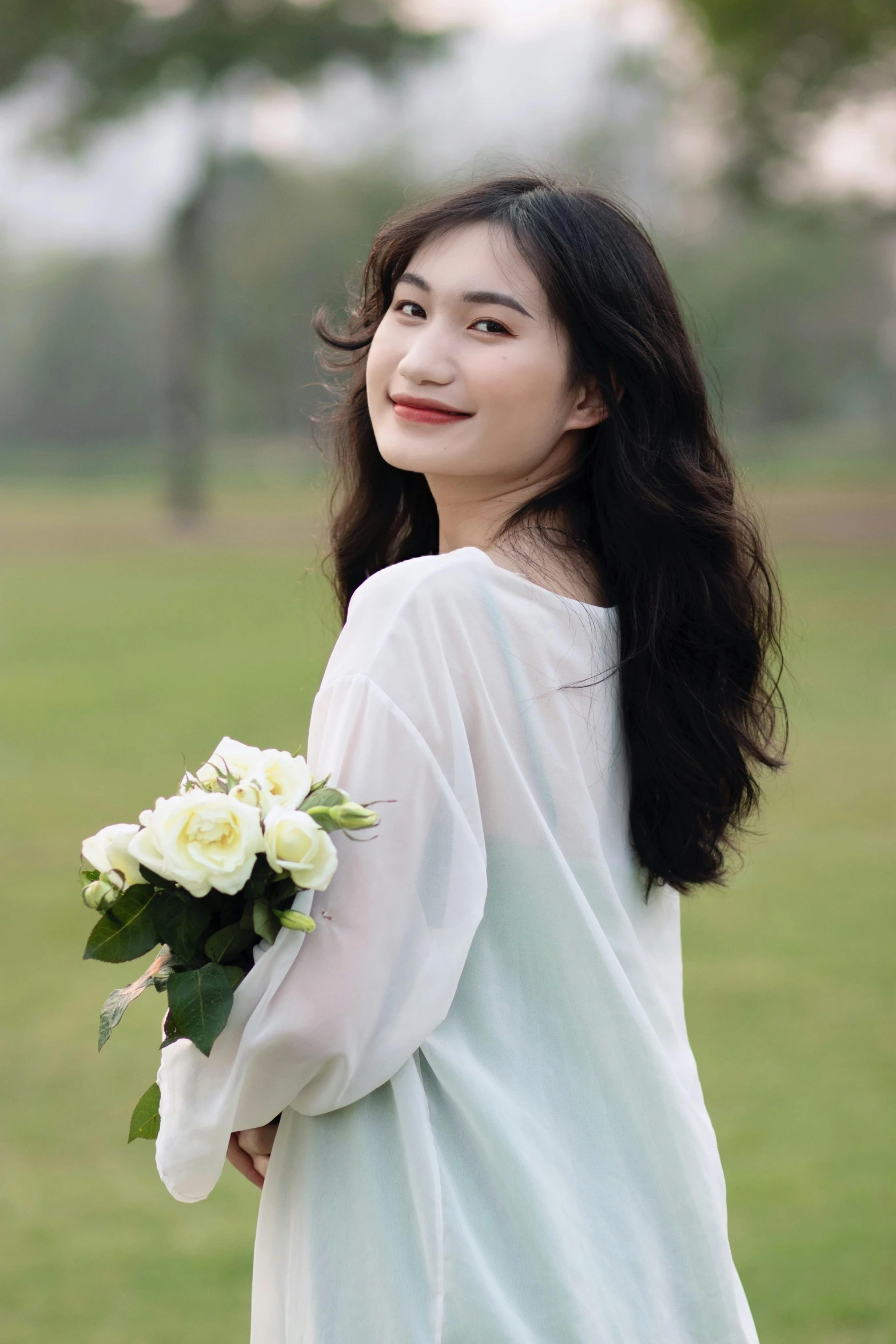 a woman holding a white bouquet of flowers in a grassy field