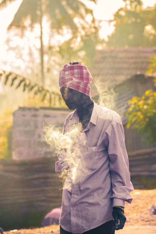 a black man stands smoking with a pink hat and checkered shirt