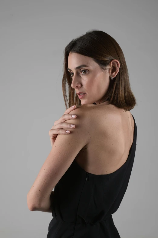 an attractive young woman in black dress with her hands on her shoulder