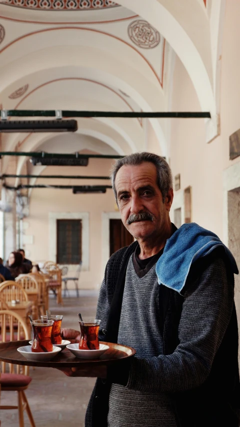 an older man with a mustache carries a tray full of drinks