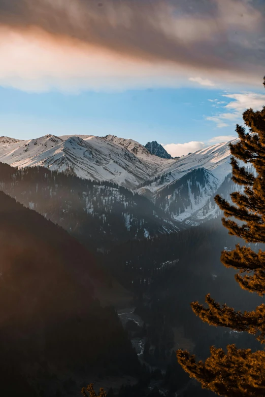 a snow capped mountain range with clouds and trees