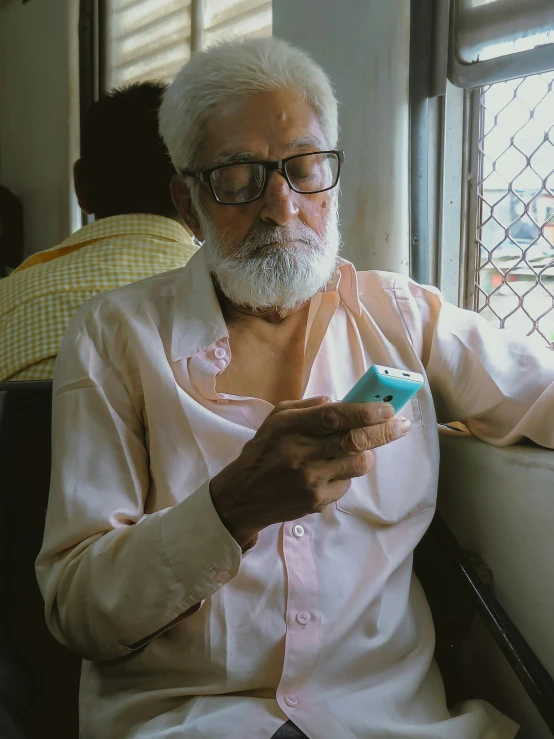 an older man sitting in a chair looking at his cell phone