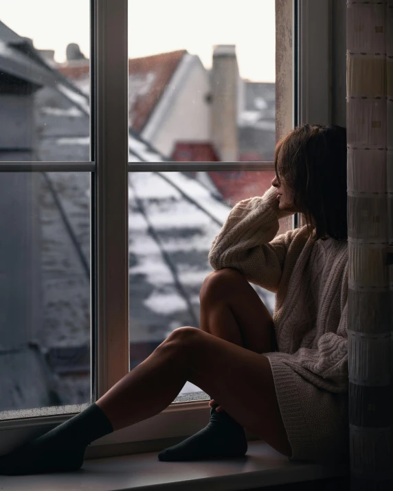 a young woman sitting on a window sill looking out at a city