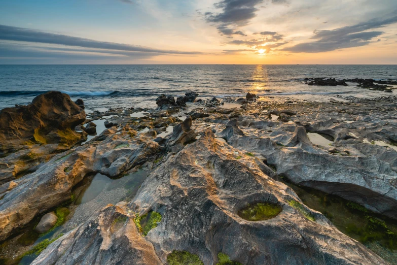 the sun is setting over an ocean with rocks